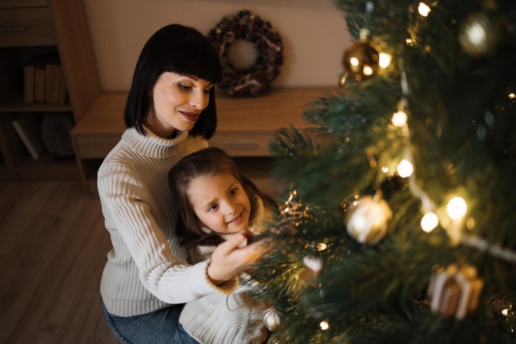 Máma a dcera zdobí vánoční stromek ve zlaté barvě